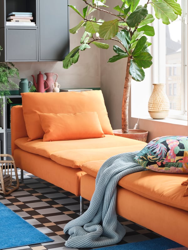Two orange chaise lounges are standing together to create a spacious day-bed, and a blue throw and a floral cushion lie here.