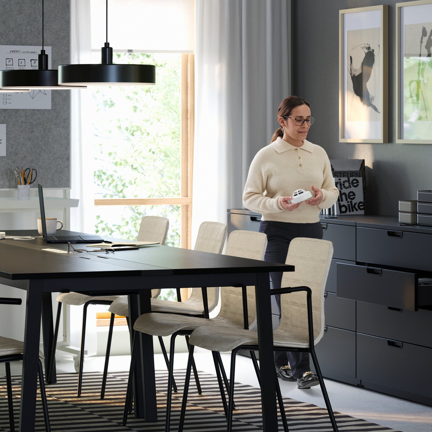 A modern meeting room with four black MITTZON conference tables, eight LÄKTARE chairs in light wood and a woman standing.