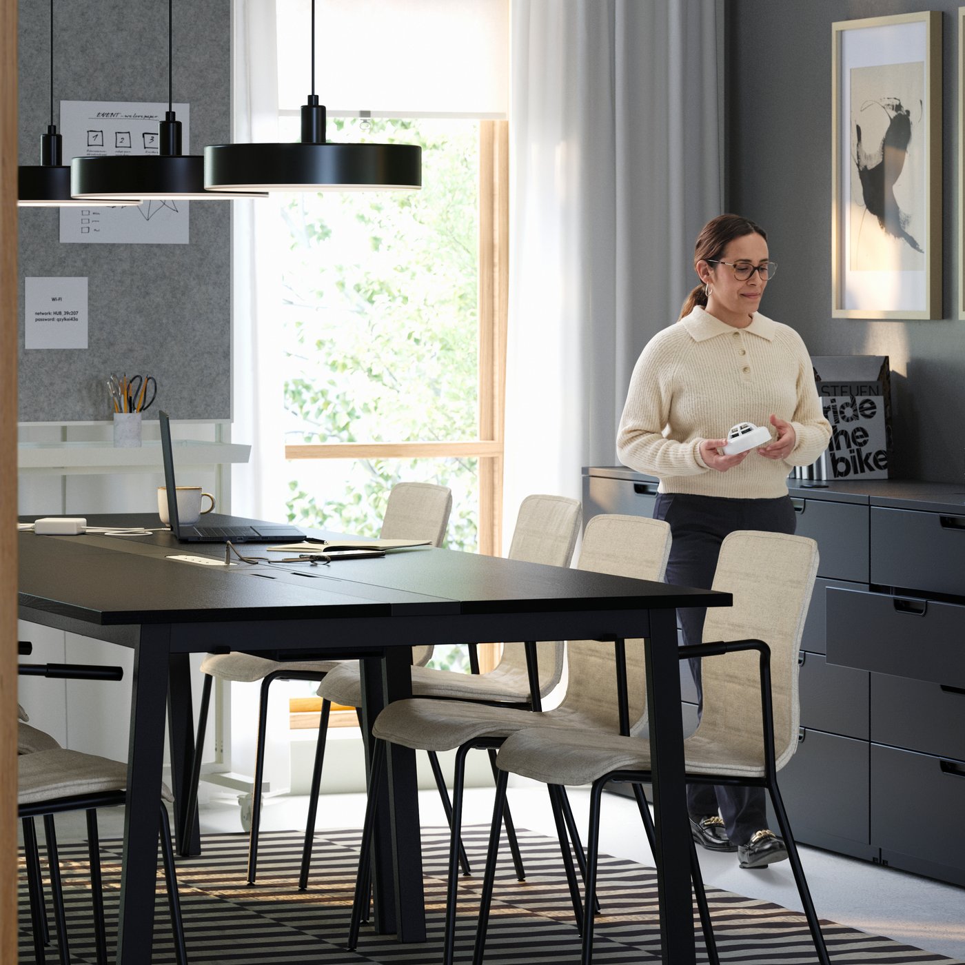 A modern meeting room with four black MITTZON conference tables, eight LÄKTARE chairs in light wood and a woman standing.