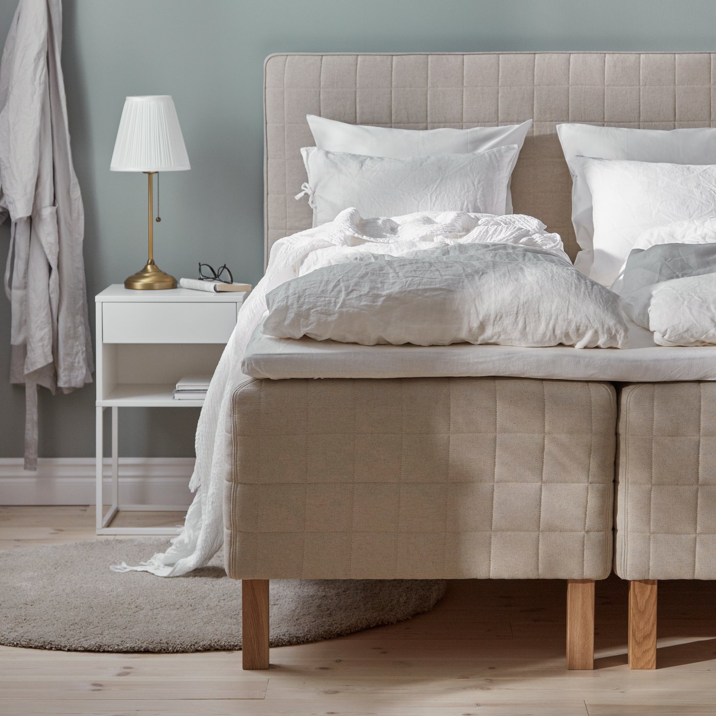 A lamp on a white VIKHAMMER bedside table next to two dressed beds with firm/natural STUVLAND spring bases.