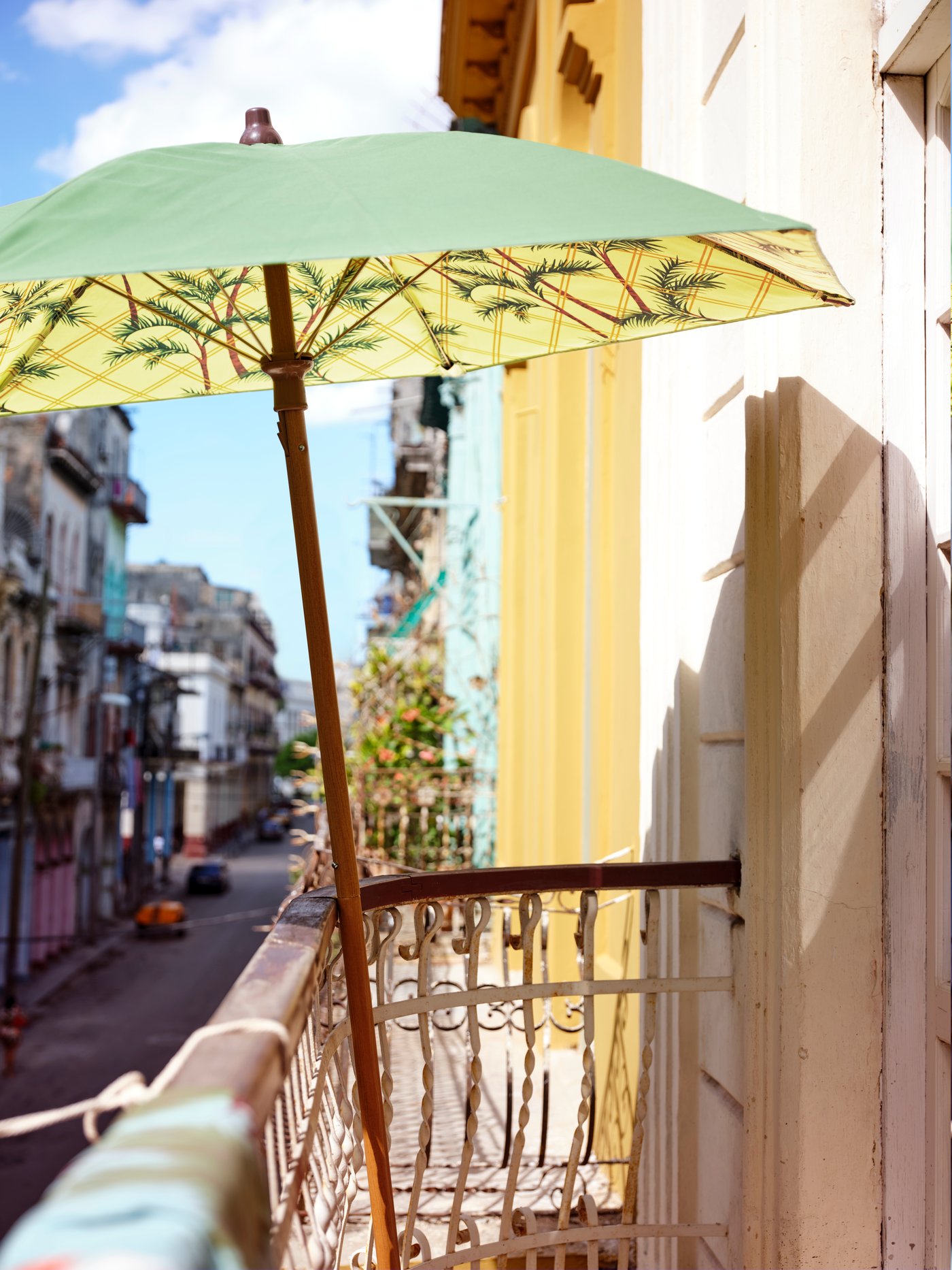 A green and yellow printed parasol leaning against a railing on a balcony above a street.