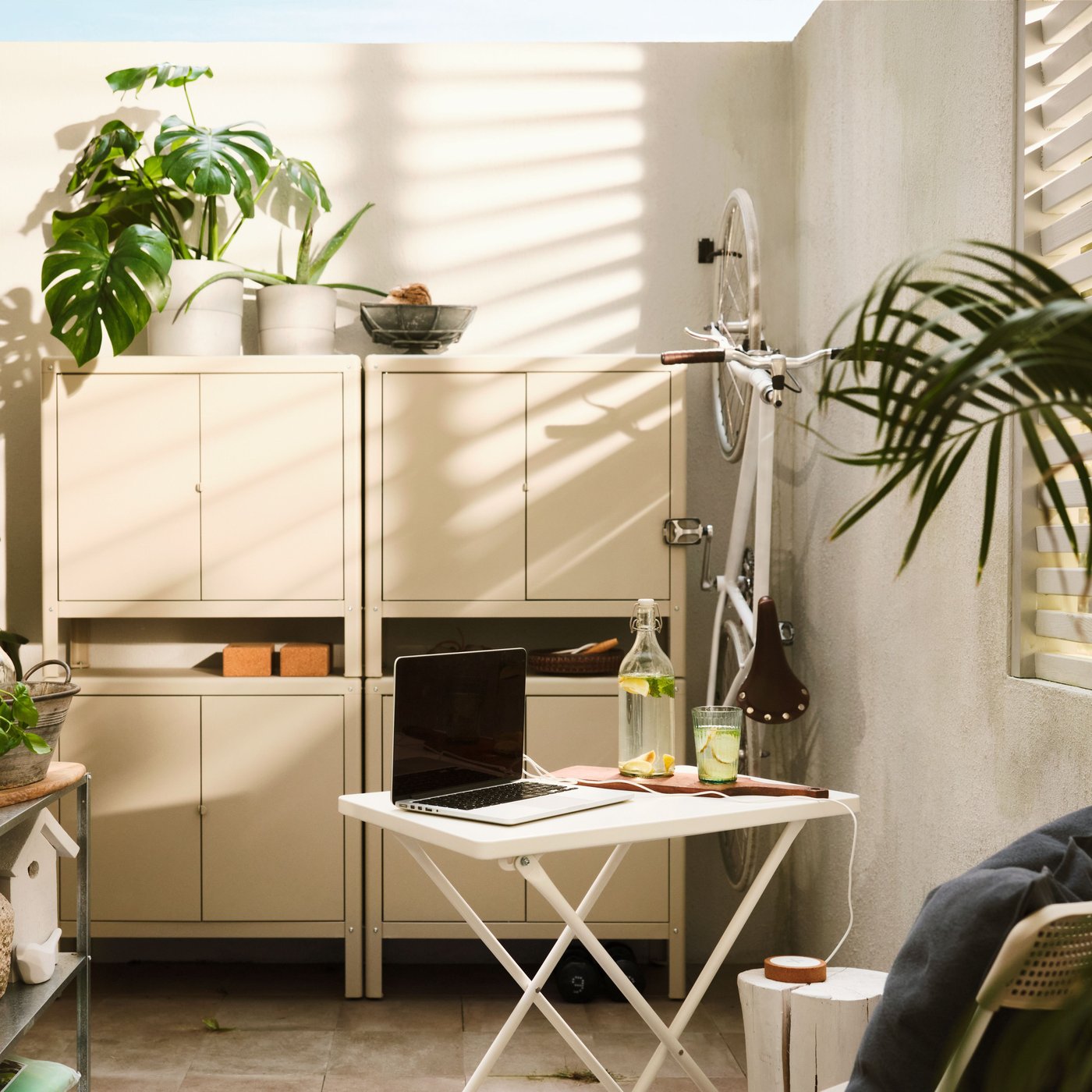 A big, beige in/outdoor KOLBJÖRN cabinet, made of two stacked cabinets on top of side-by-side cabinets, is on a balcony wall.