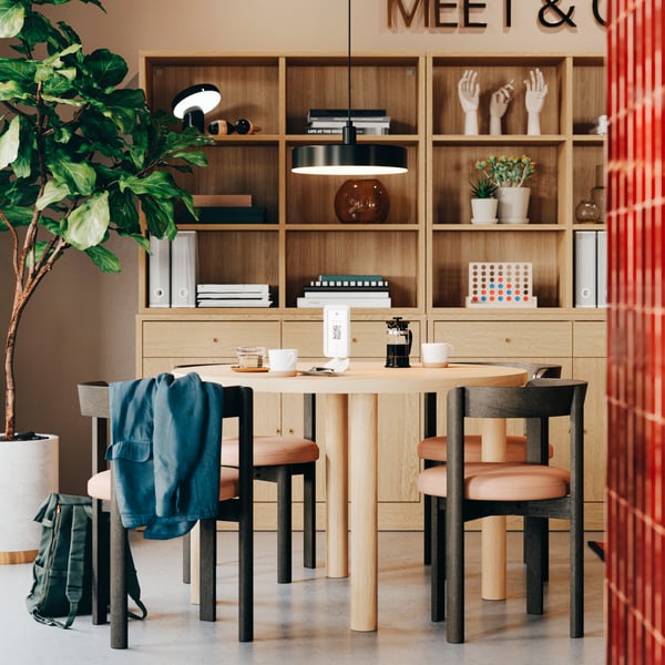 Hotel lobby area featuring a STOCKHOLM 2025 oak table with four dark brown chairs and oak veneer shelves in the background.