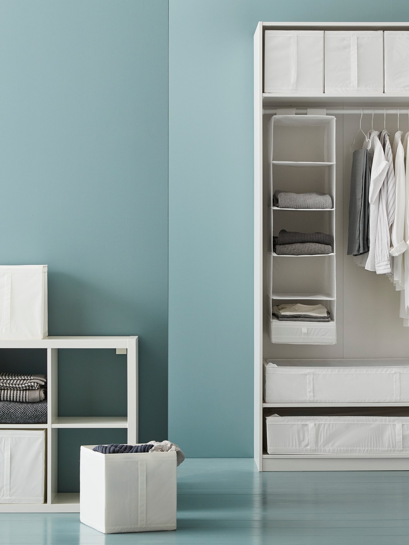 Dormitorio con una caja junto a una estantería y una estructura de armario blanca con compartimentos y cajas de almacenaje.