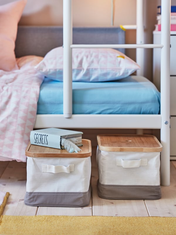 RABBLA boxes with lids, which have been pulled out from underneath a VITVAL bunk bed, sit on the floor beside the bed.