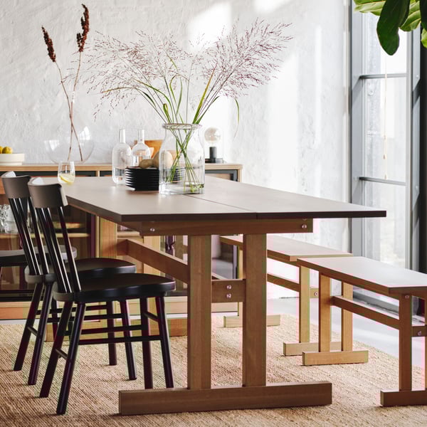 Two grey-brown KLIMPFJÄLL benches and some black NORRARYD chairs stand at a grey-brown KLIMPFJÄLL dining table.