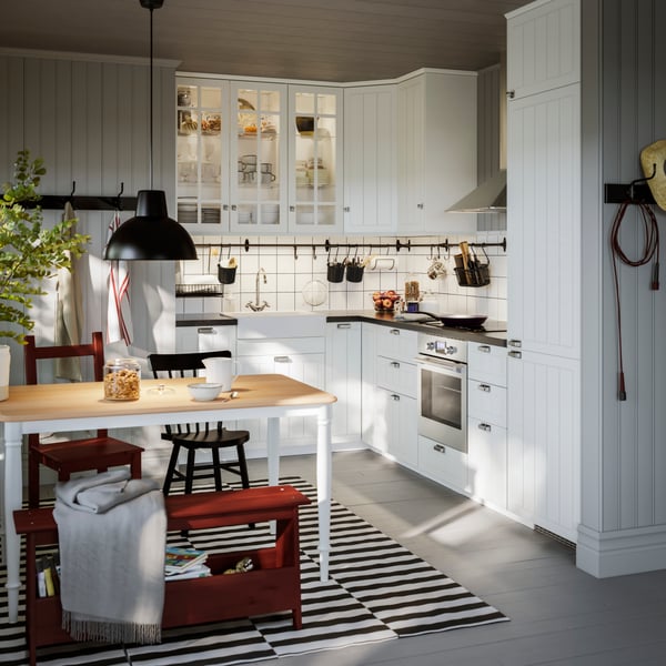 Et hvidt hjørnekøkken med låger i traditionel stil ved siden af en spiseplads oven på et stribet gulvtæppe.