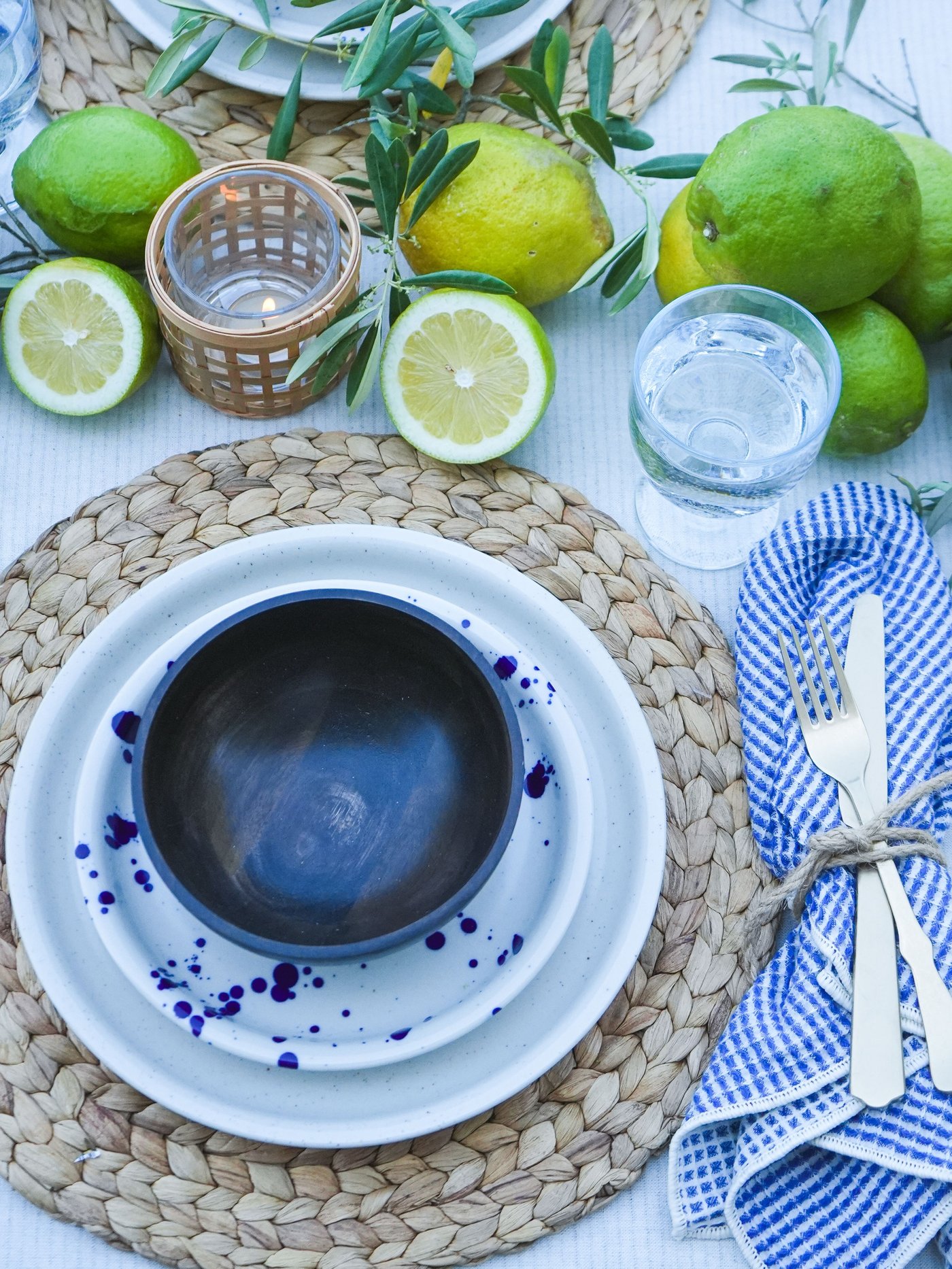 Une table estivale agrémentée de citrons frais, de brins d'olivier, de vaisselle SILVERSIDA bleue et blanche et de couverts rustiques.