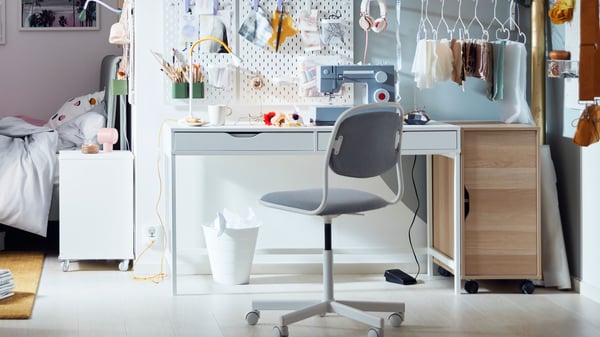A bright, colourful room with pegboards over an ALEX desk, and curtains and a KALLAX shelving unit sectioning off a bed.