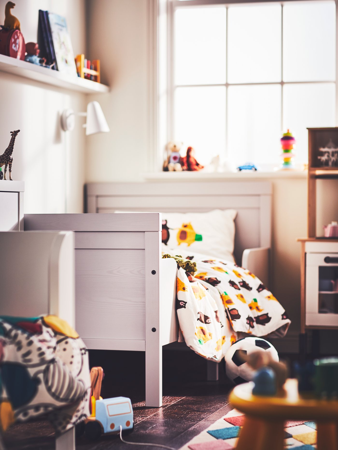 A children’s room with a white FUBBLA LED wall lamp above a grey SUNDVIK extendable bed with a duvet, pillow and bedding set.