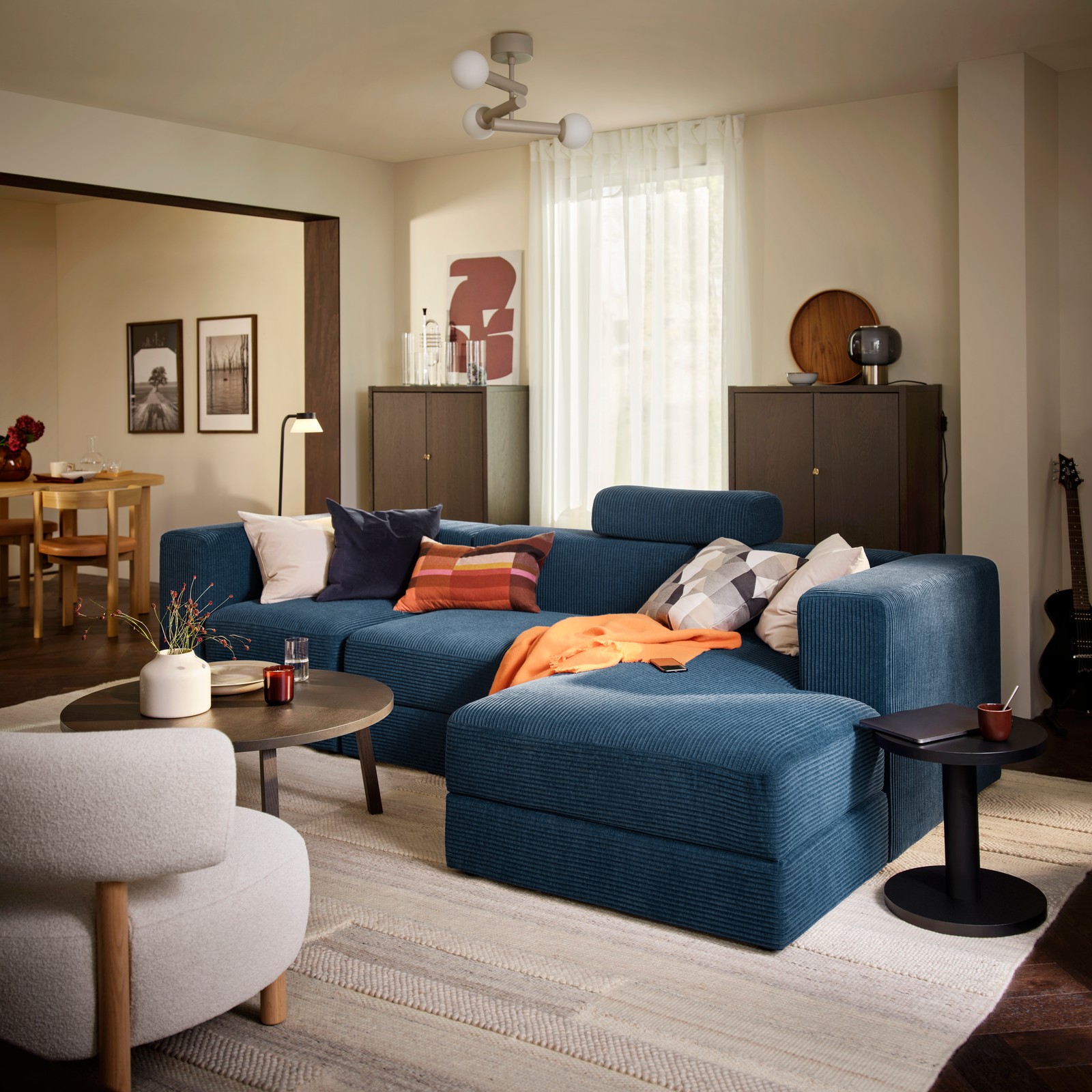 A living room with a dark-blue JÄTTEBO four-seat sofa with chaise longue, complemented by a round table and decorative items.