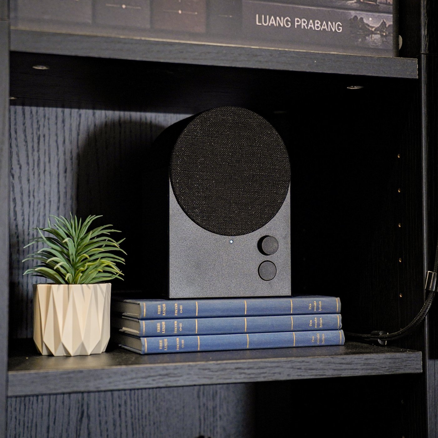 Curious Library room setting at IKEA Tampines, featuring a black NATTBAD bluetooth speaker is placed within the shelf of a black oak effect BILLY bookcase.
