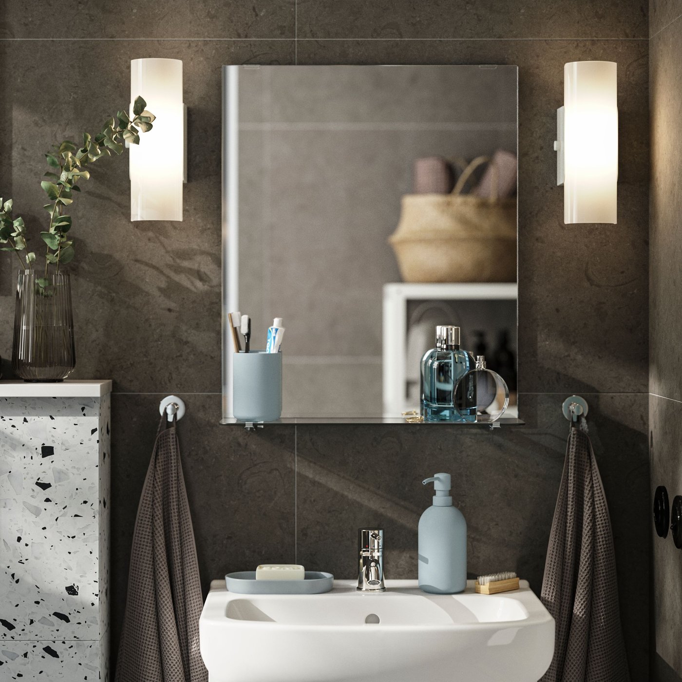 Obdélníkové zrcadlo NYSJÖN s policí z skla na kartáčky a lahvičky parfémů nad bílým umyvadlem a skříňkou.