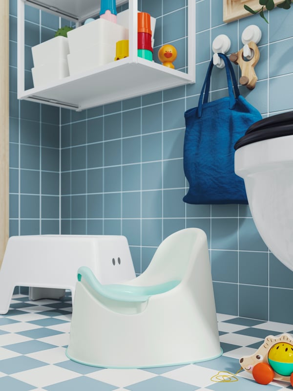 A turquoise LOCKIG children’s potty and a white step stool are placed on a checkered bathroom floor in white and turquoise.