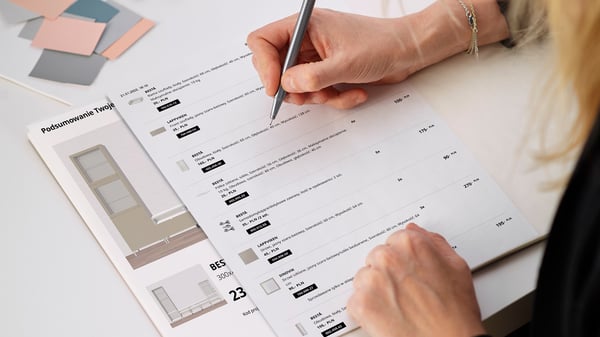 Kartki z wydrukiem projektu szafek BESTÅ i listą zakupów, na których kobieta nanosi notatki.