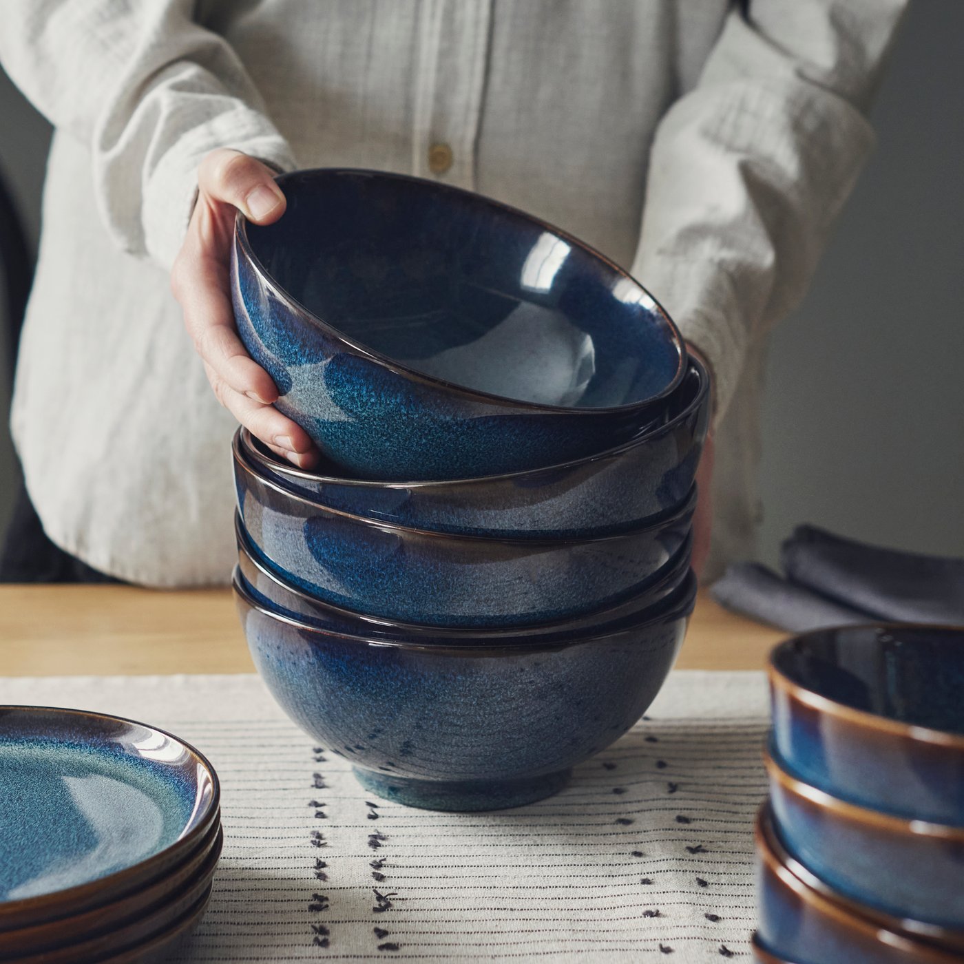 Een stapel blauwe GLADELIG schaaltjes met daarnaast een stapel blauwe GLADELIG borden op een tafel.