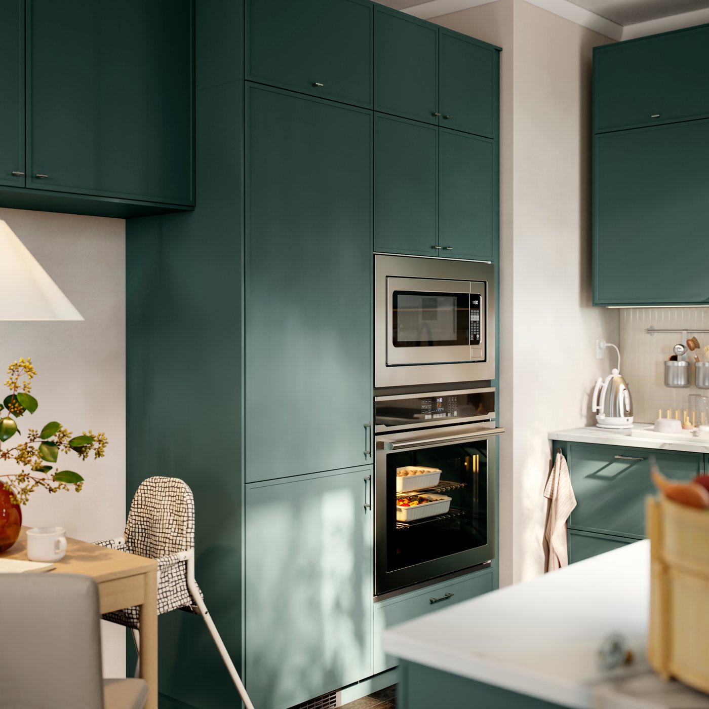 A high cabinet for built-in appliances with grey-green doors has an integrated oven and microwave, with drawers below.