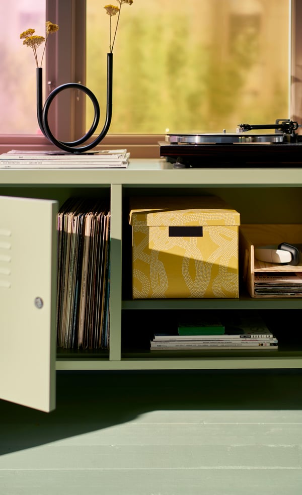 A green IKEA PS cabinet stands in a student’s bedroom, with one door open showing film boxes displayed on the inside.