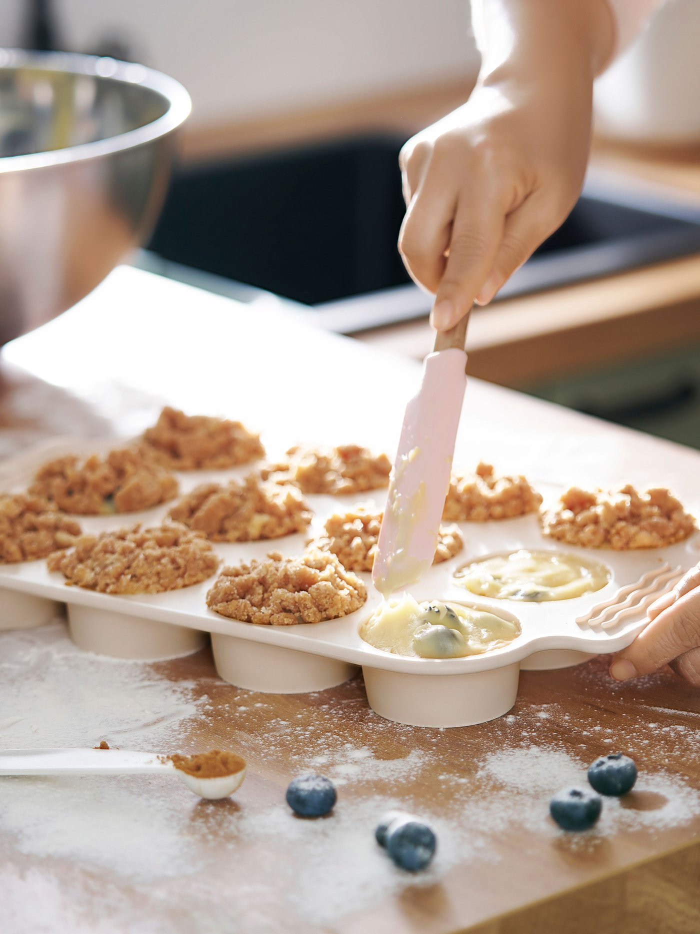 Osoba nakładająca ciasto do beżowej formy do muffin BAKTIDER.