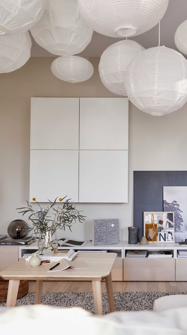 BESTÅ low TV bench with open storage slots and closed drawers, in a living room with lots of hanging lamps in white.