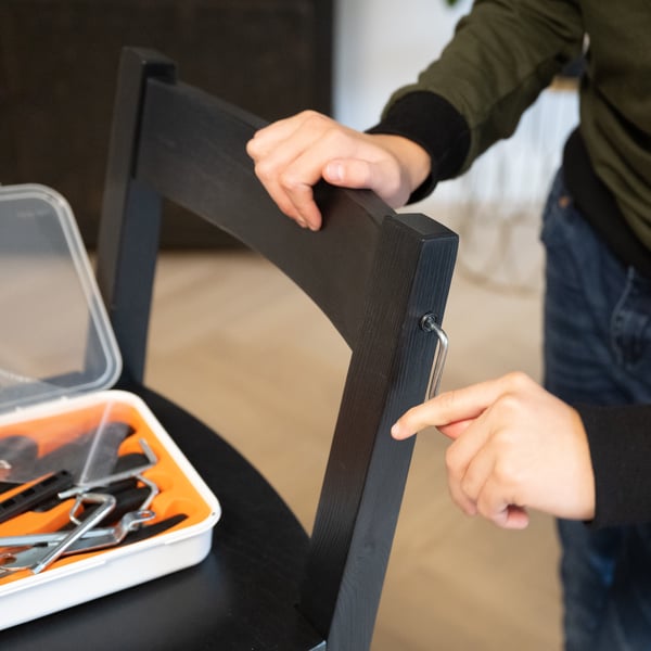 A man repairing a wooden chair by replacing one of the lateral screws 