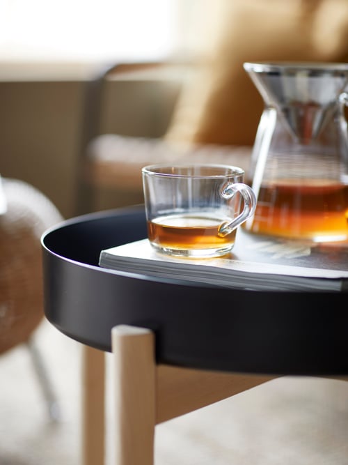 Cameră de zi cu măsuță de cafea rotundă, cană de sticlă care conține cafea, cafetieră pentru cafea, un scăunel pentru picioare și un fotoliu.