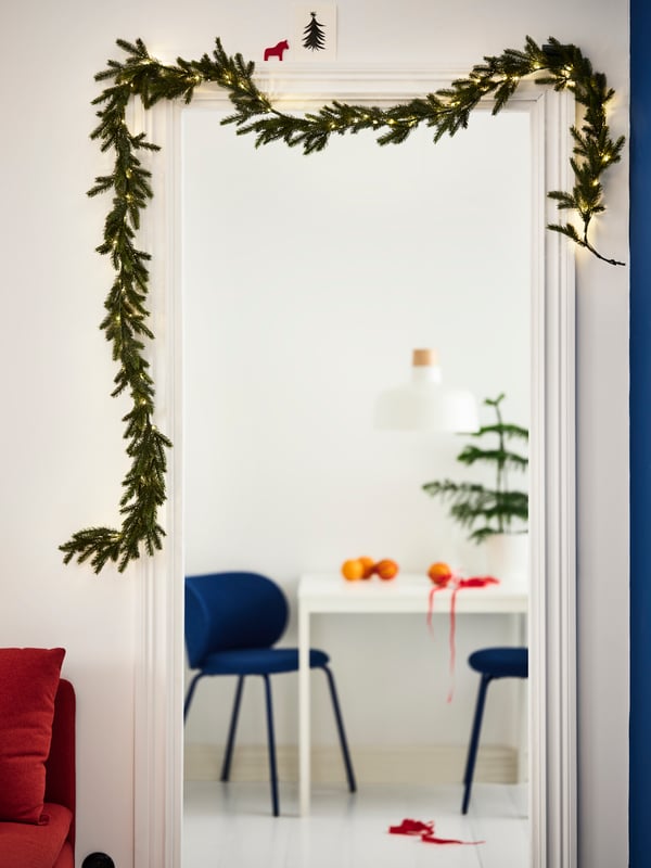 A doorpost decorated with a battery-operated STRÅLA LED artificial garland – an evergreen wreath with built-in lighting.