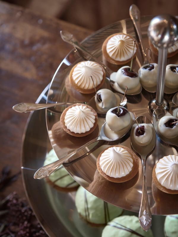 Varias cucharas INBJUDEN con cerezas bañadas en chocolate blanco dispuestas en una fuente para servir en pisos INBJUDEN.