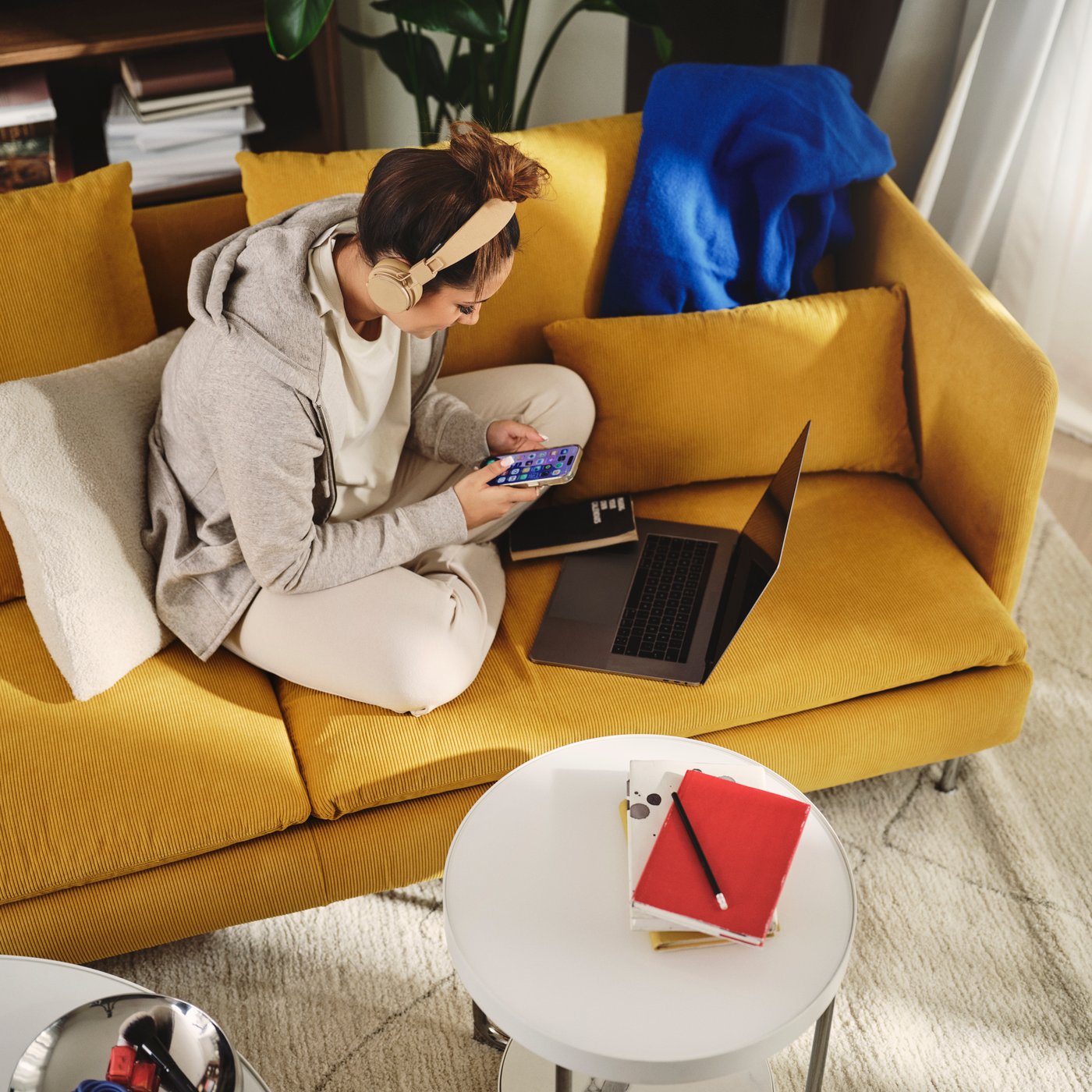 A living room with a dark yellow SÖDERHAMN 4-seat sofa-bed beside a laptop and a coffee table with notebooks.