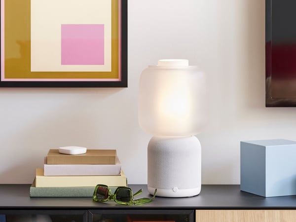 A SYMFONISK table lamp with WiFi speaker in white/grey placed on a black cabinet.