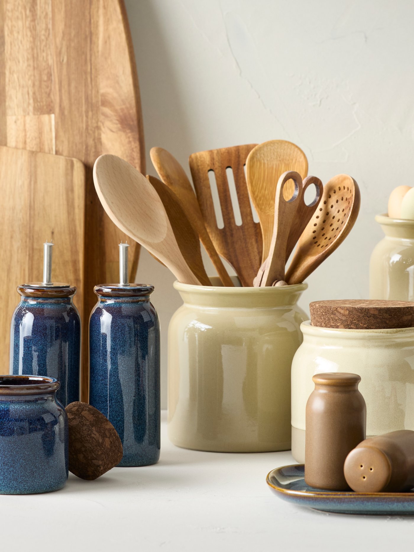 A blue BRUGDHAJ jar with a cork lid next to it is placed next to two blue BRUGDHAJ oil and vinegar bottles on a worktop.