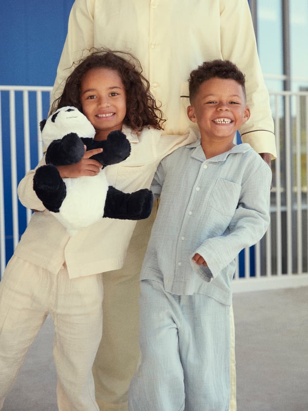 Two smiling children in pyjamases are hugging each other, one of them is holding a DJUNGELSKOG soft toy in her arms.