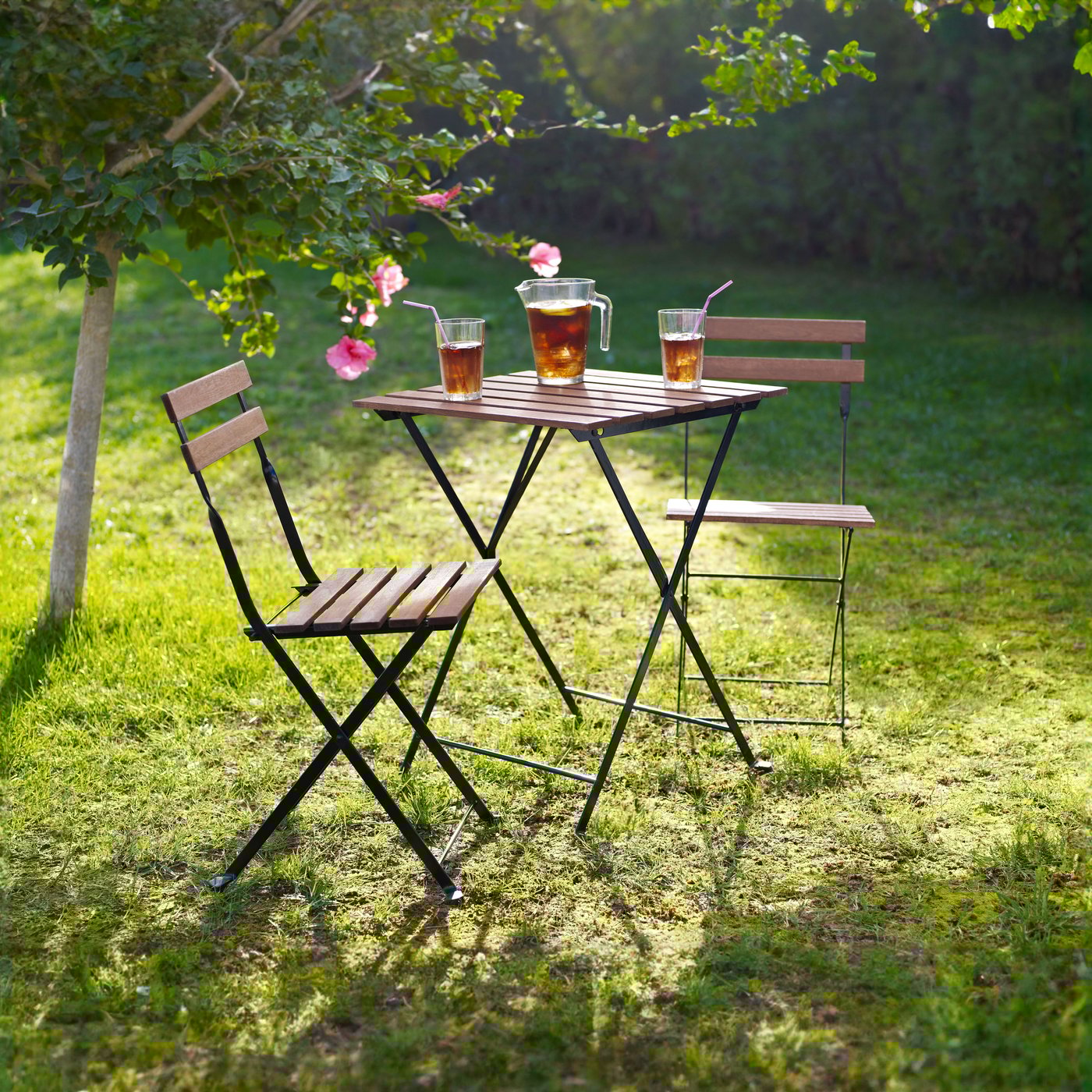 TÄRNÖ-pöytäryhmä puutarhassa, pöydällä mehukannu ja kaksi lasia.