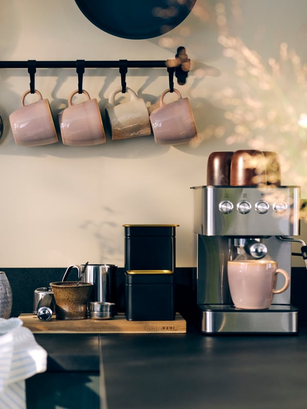 Une cuisine avec un plan de travail sur lequel sont posés divers appareils de cuisine et des tasses FÄRGKLAR suspendues à un support mural.