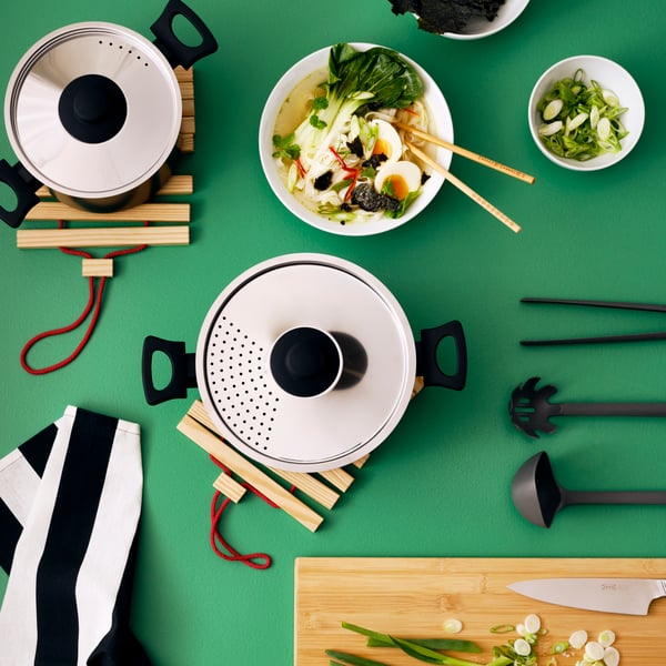 An APTITLIG chopping board in bamboo, ANNONS cookware in stainless steel and IKEA 365+ deep plate and bowl with food in them.