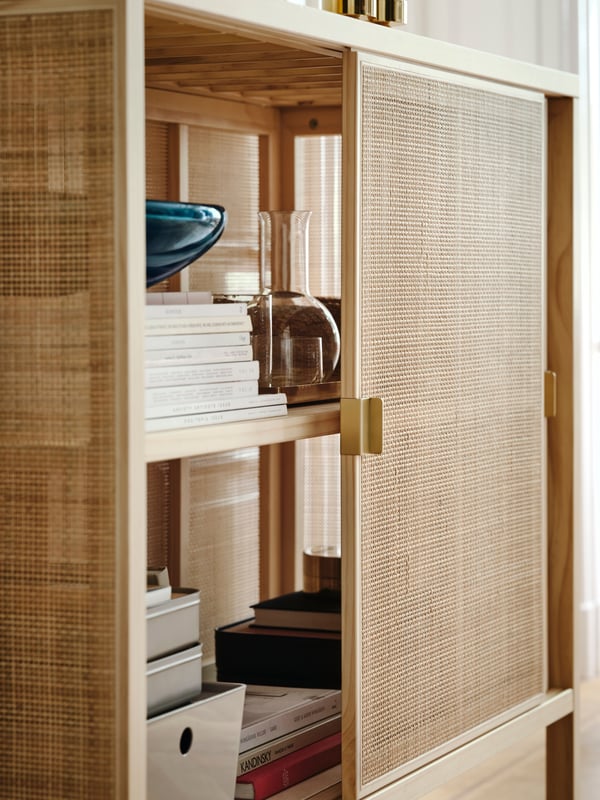 A door of a STOCKHOLM 2025 cabinet with sliding doors is partly open, showing a carafe and a bowl on a shelf inside.