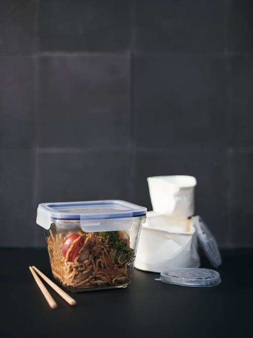 Kitchen close-up of a transparent grey food container with leak-proof lid, made out of durable plastic next to chopsticks.