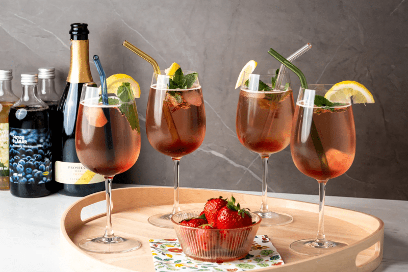 4 Weingläser, die gefüllt sind mit dem nordischen Sommerspritzer und auf einem Tablet stehen.