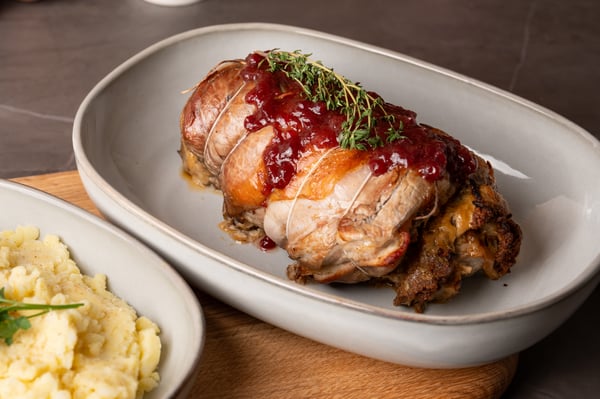 Gerollte Kalbsbrust mit Preiselbeer-Glasur und Kartoffelpüree auf einem weißen Geschirr serviert.