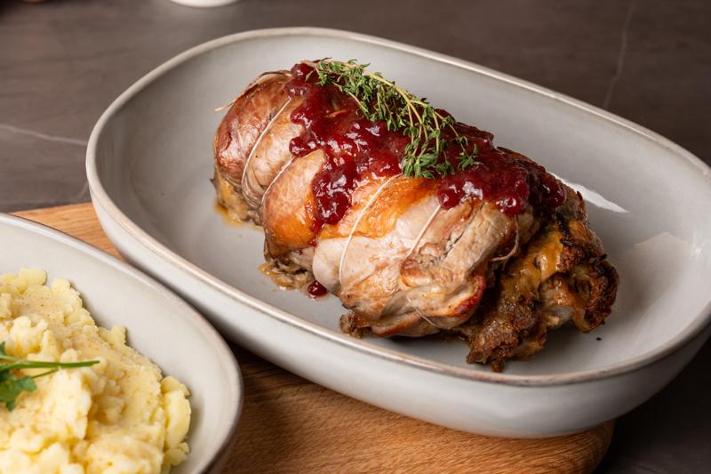 Gerollte Kalbsbrust mit Preiselbeer-Glasur und Kartoffelpüree auf einem weißen Geschirr serviert.