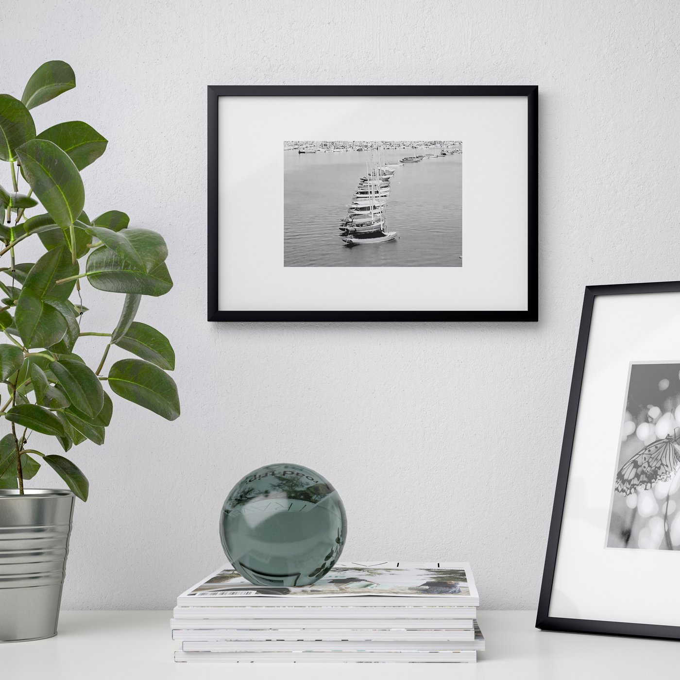 One LOMVIKEN frame mounted on a wall, and another one standing on a bench top beside some magazines and a plant.