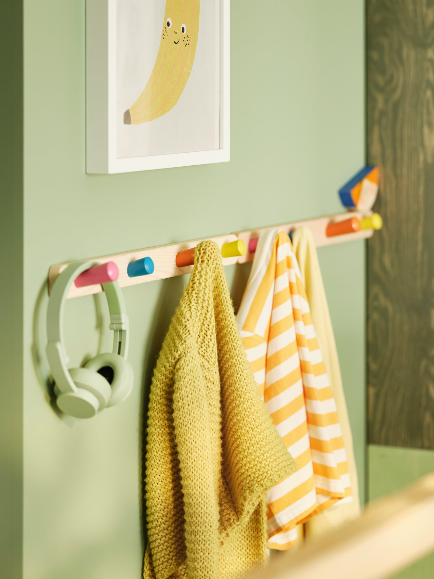 カラフルなFLISAT/フリサット ノブラックに掛けた子ども服のクローズアップ。その上の壁にはバナナのアートが掛かっている。