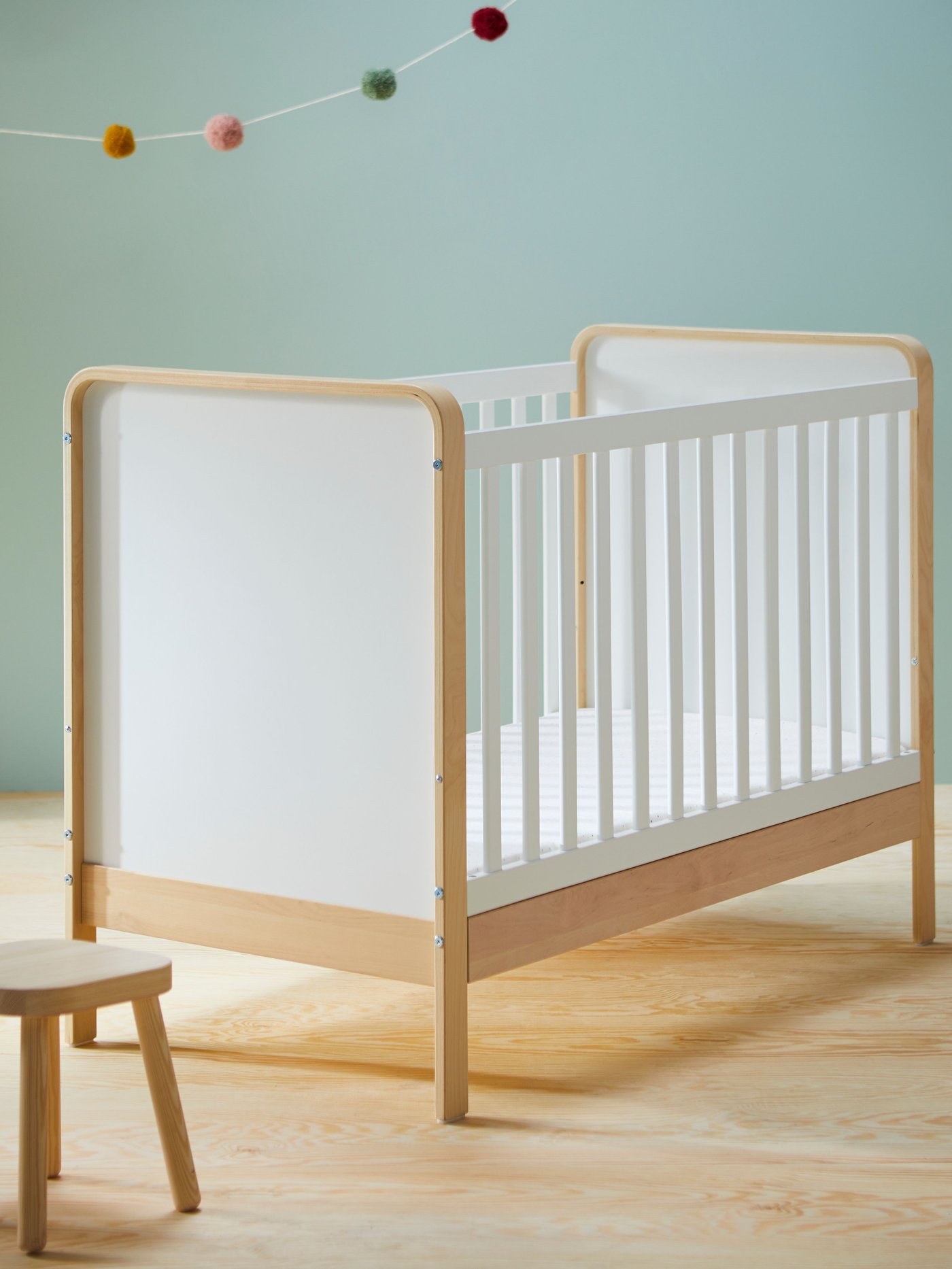 A baby cot in a blue room with hanging lights and a wooden stool