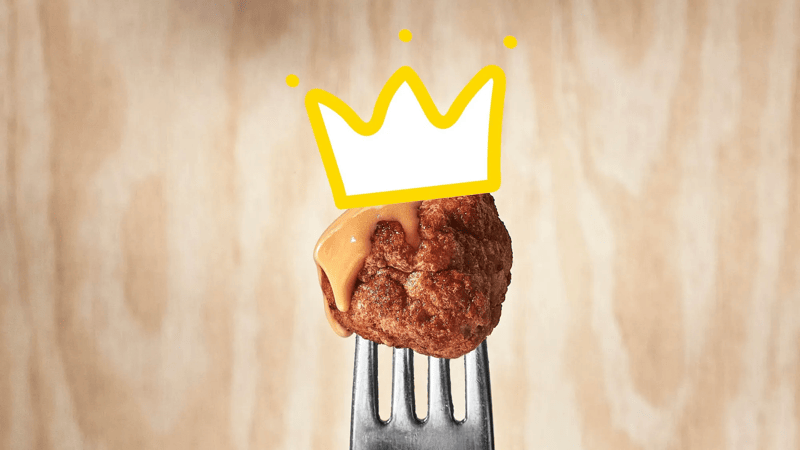 A fork with a single meatball with gravy wearing a crown.