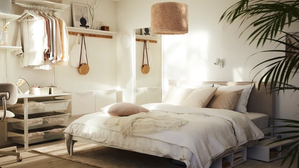 Ein helles Schlafzimmer mit einem KLEPPSTAD Bettgestell und weißer ÄNGSLILJA Bettwäsche. Darüber hängt eine LERGRYN Leuchte.