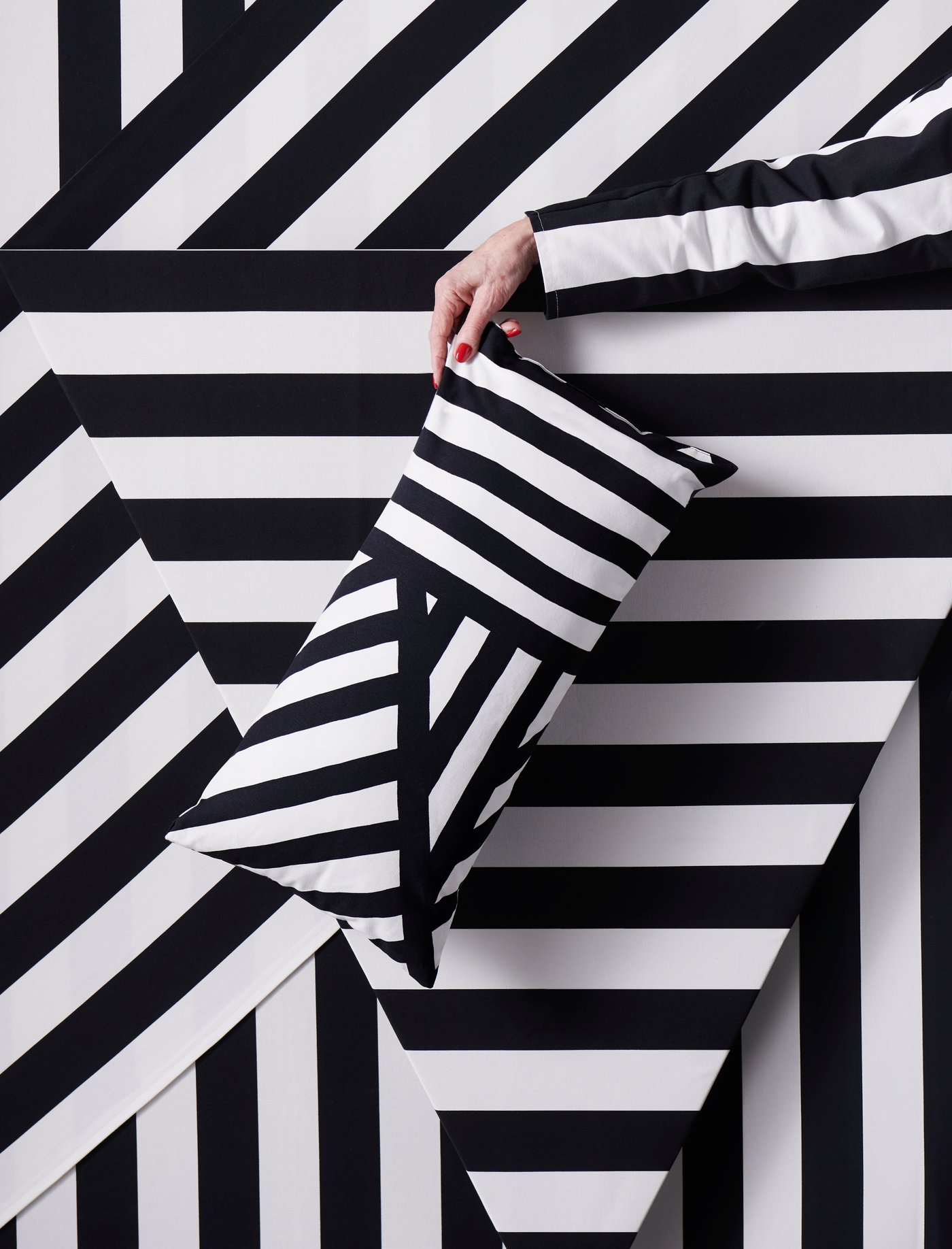 Black and white striped SOFIA fabric in different cuts and a person holding a black and white cushion in front of it.