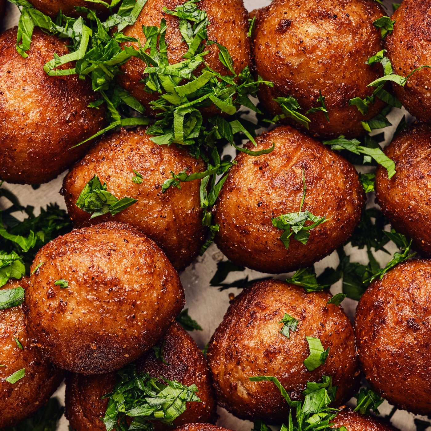 Plusieurs boulettes végétales HUVUDROLL dorées garnies d’herbes aromatiques fraîches, prêtes à être servies.