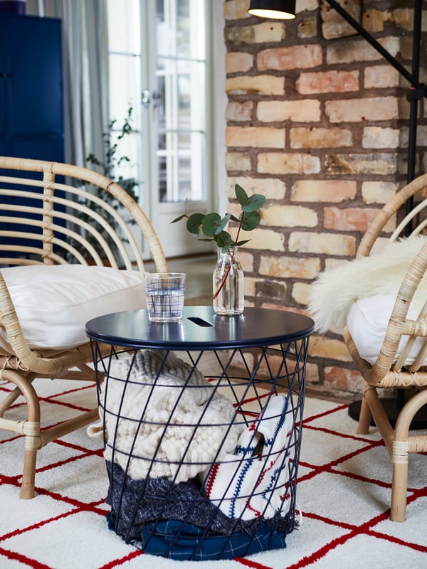 Terraza con dos sillas y una mesa de centro con almacenamiento en su interior. Sobre ella hay un vaso con agua y un florero.