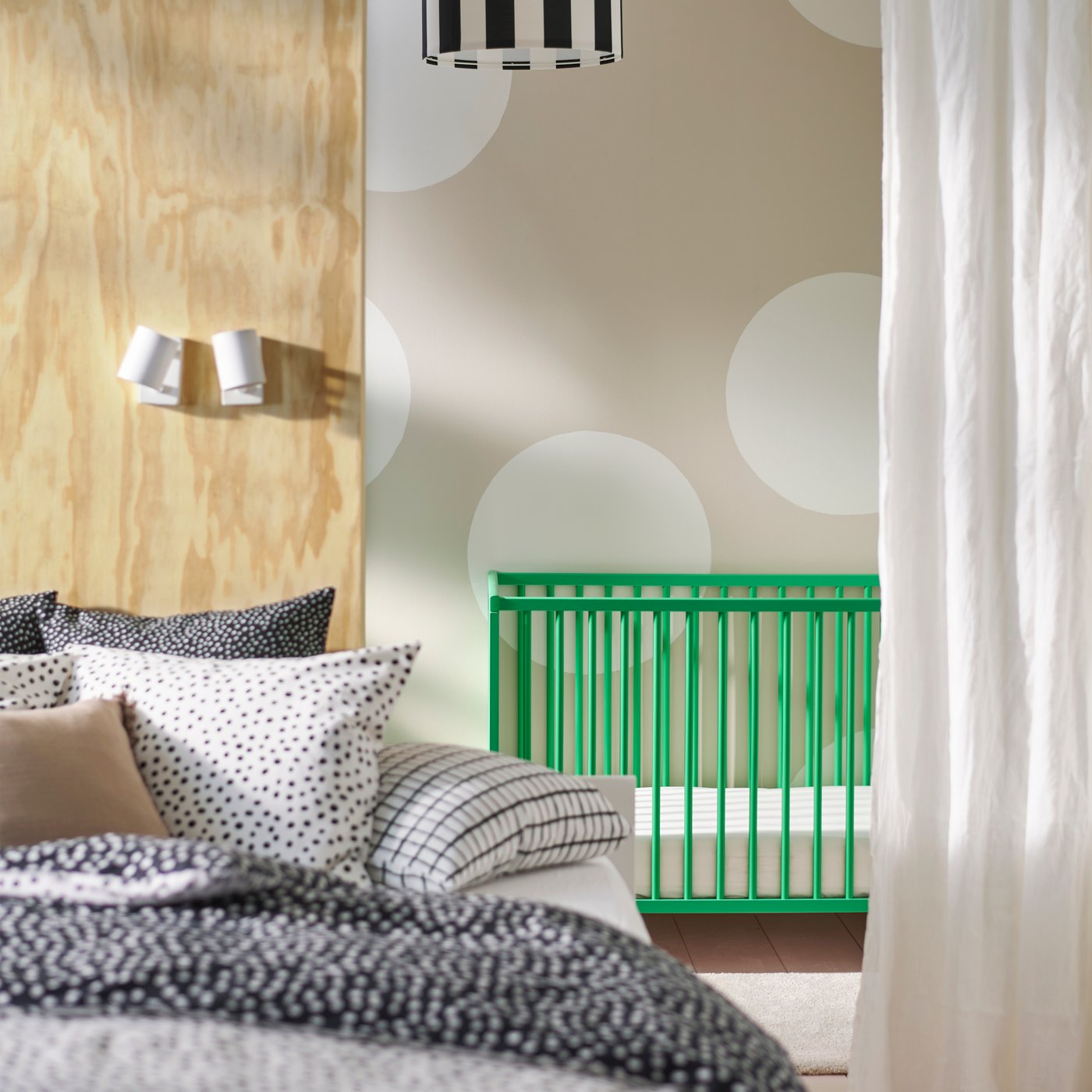 A green GULLIVER cot is placed against a light-coloured polka-dot wall. A bed covered in BJÖRKGRÅMAL bed linen is in front.