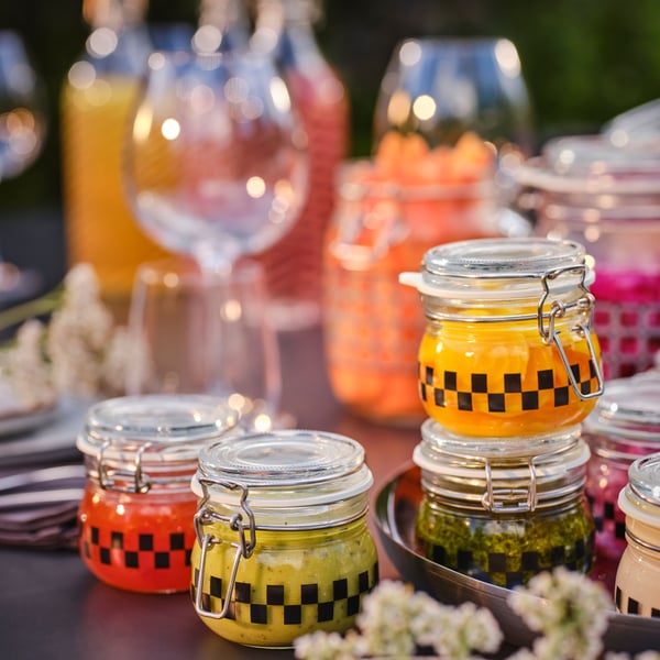 Detalle de varios tarros con diferentes salsas colocados sobre una mesa alrededor de copas y comida.